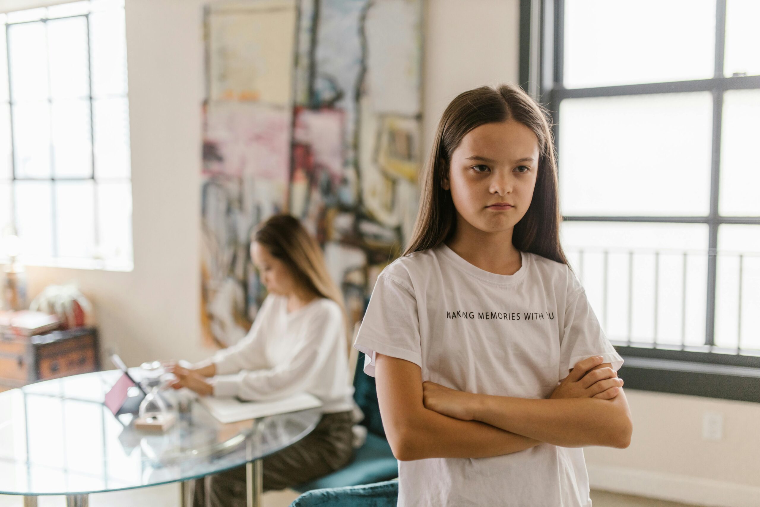 A young girl looks displeased with crossed arms in a modern indoor setting.