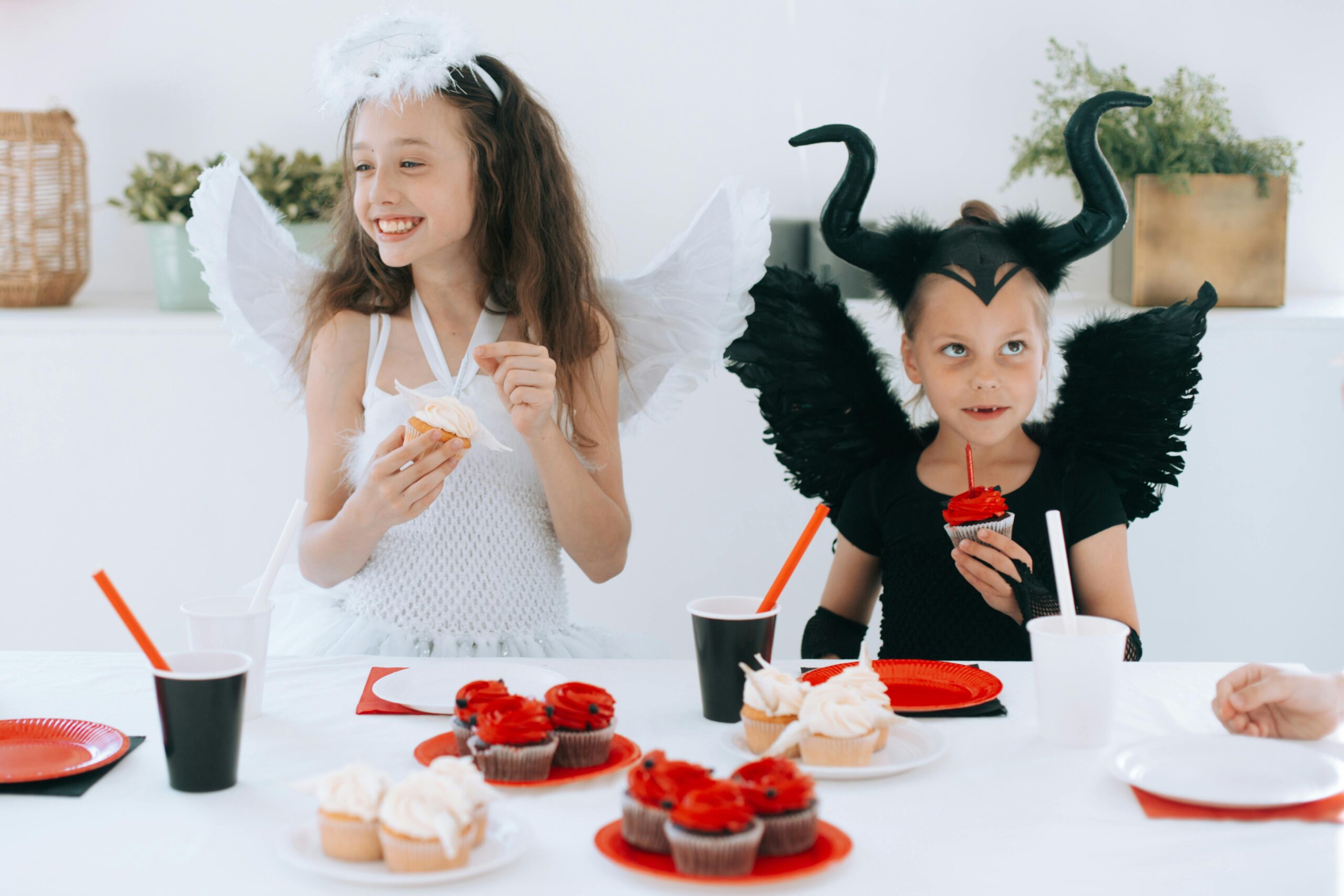 Kids dressed as angel and devil enjoy cupcakes at a Halloween party.